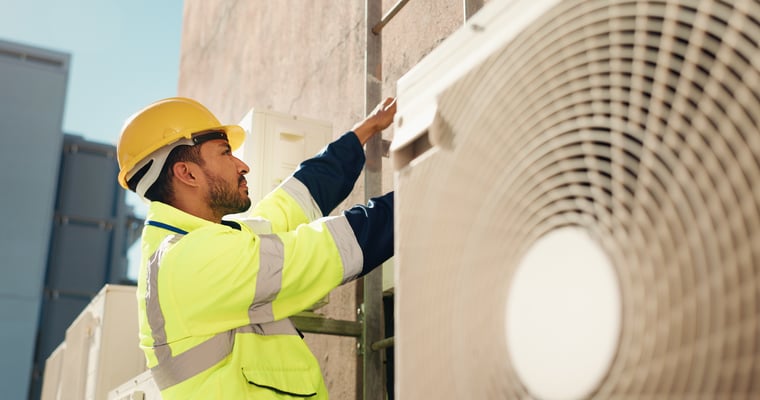 HVAC technician working outdoors in the city, performing air conditioner installation, maintenance, repair, and inspection.